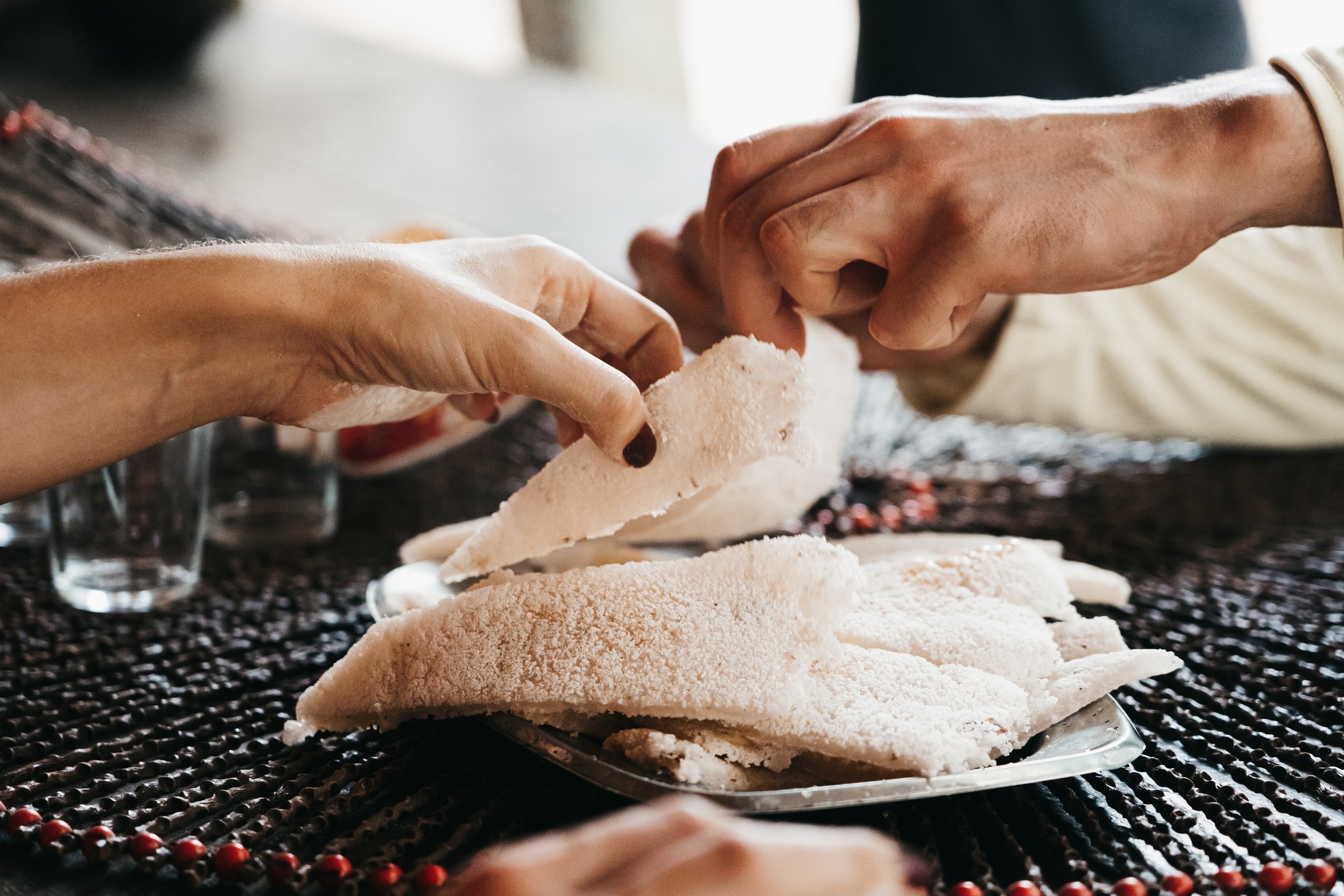 Two people breaking apart a piece of soft white cassava flatbread over a shared plate on an untamed amazon cruise meal table