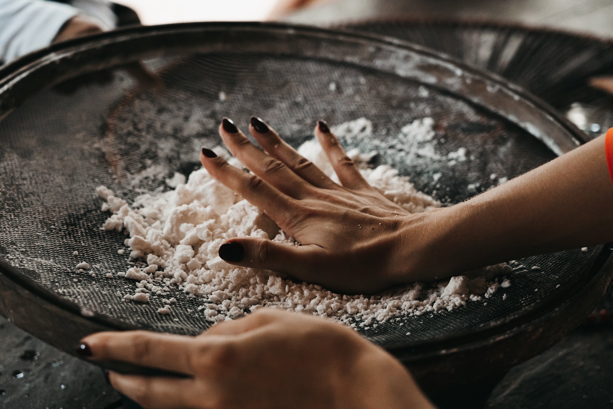 Hands pressing grated cassava through a large wire sieve during a community visit on the untamed amazon cruise