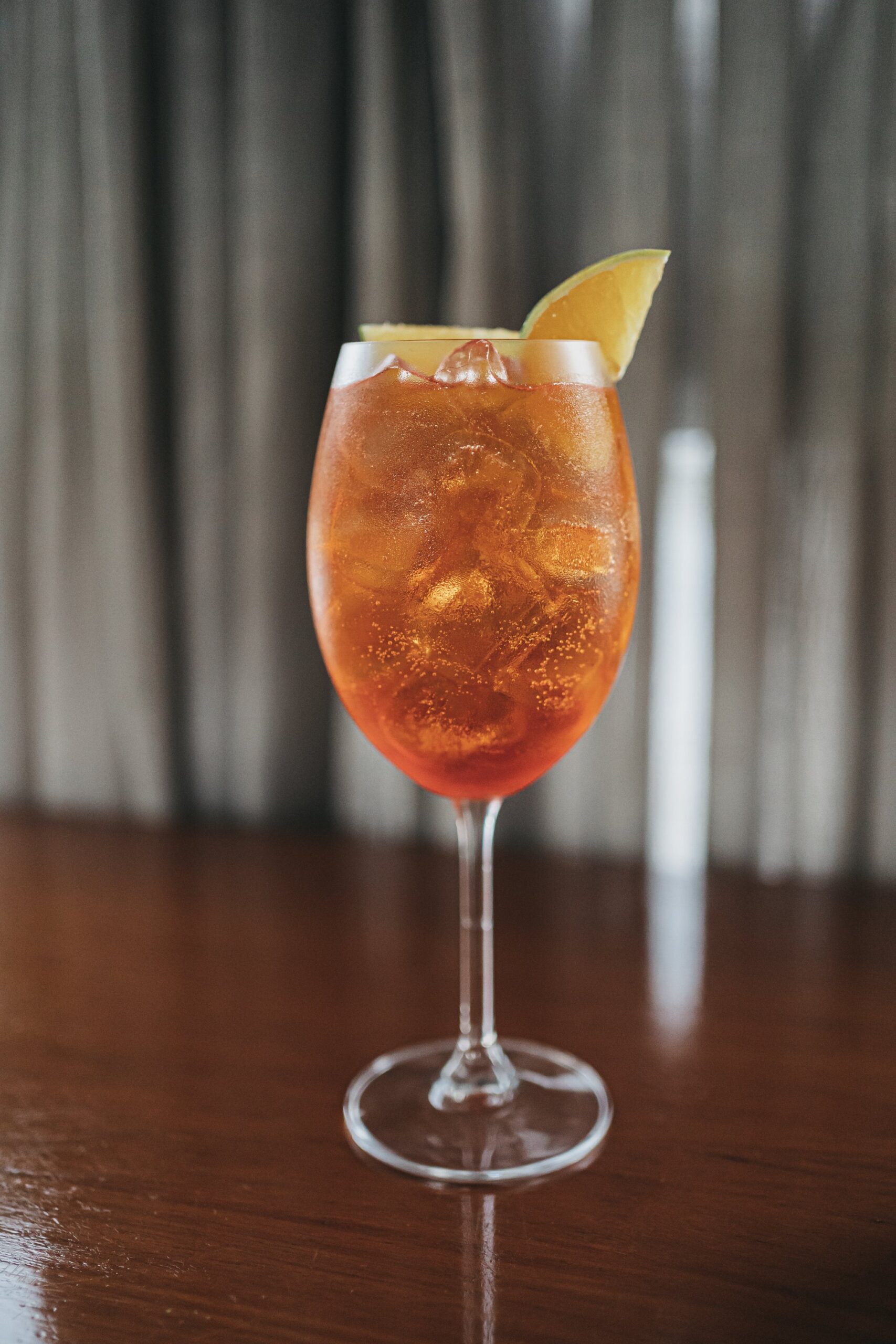 An amber iced cocktail in a stemmed wine glass garnished with a citrus wedge, served on a dark wood bar aboard the untamed amazon cruise