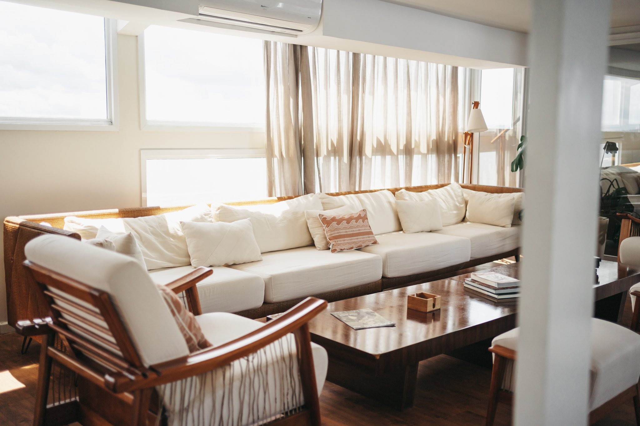 Sunlit social lounge on the untamed amazon cruise featuring a wide cream sofa with rattan frame, wooden armchairs, and a polished coffee table beneath sheer linen curtains