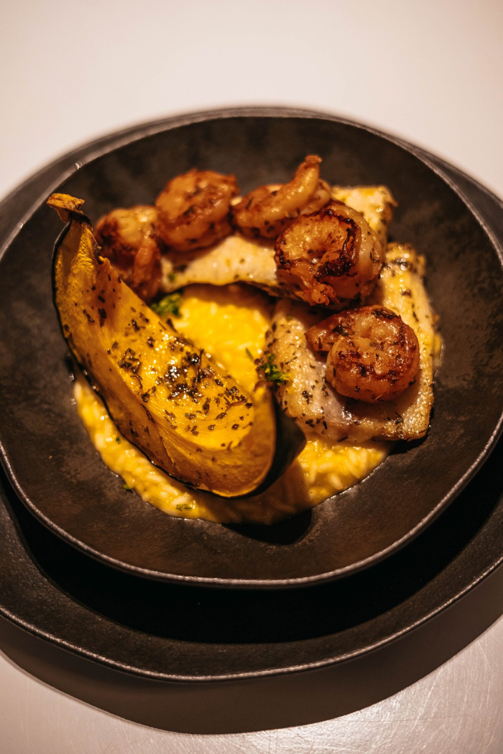Seared shrimp and white fish fillet plated on a golden cream sauce with a charred plantain half, served in a matte black bowl on the untamed amazon cruise