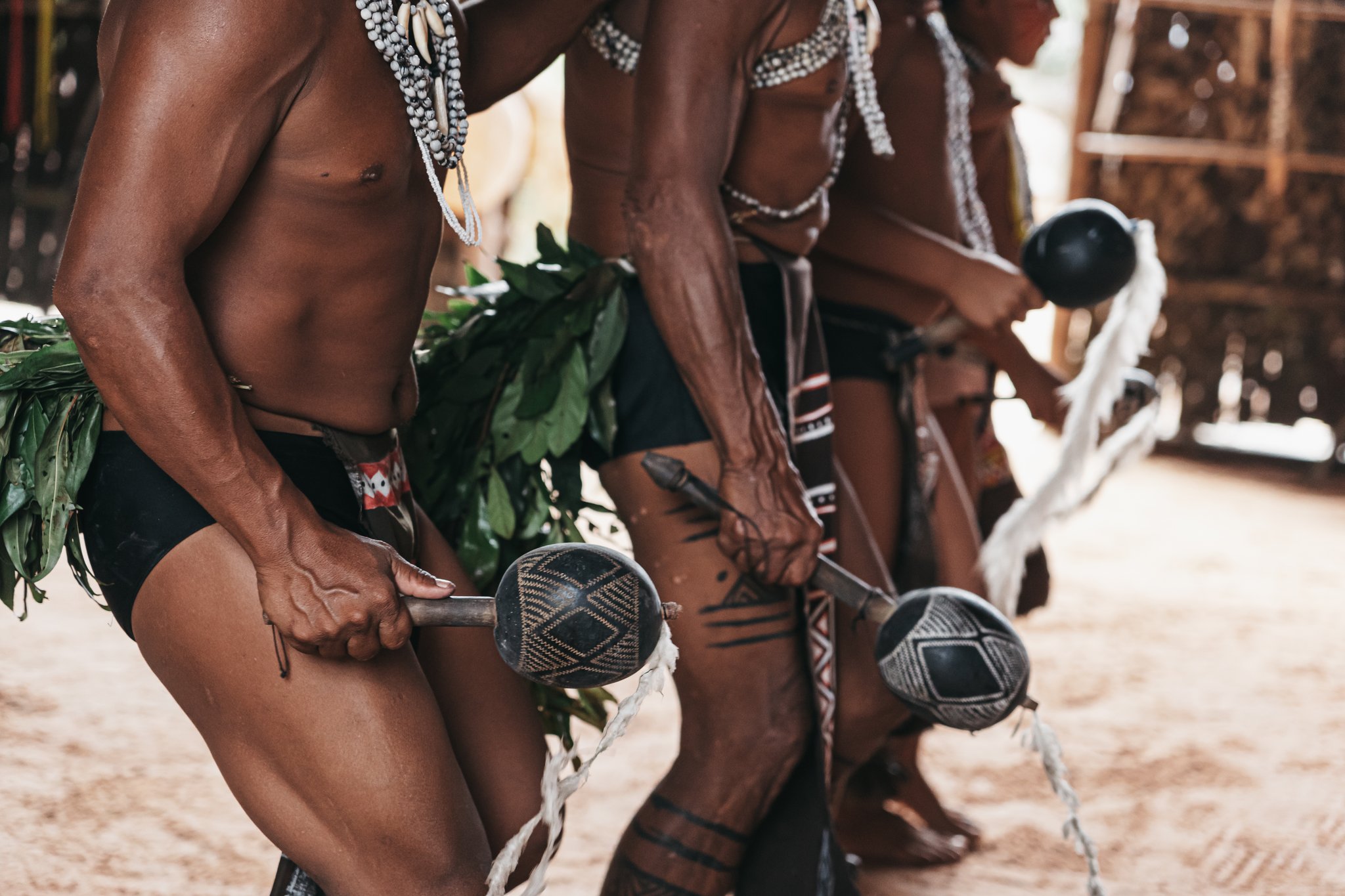 Close-up of indigenous men holding decorated gourd rattles with geometric patterns during a ceremony on the untamed amazon cruise community visit