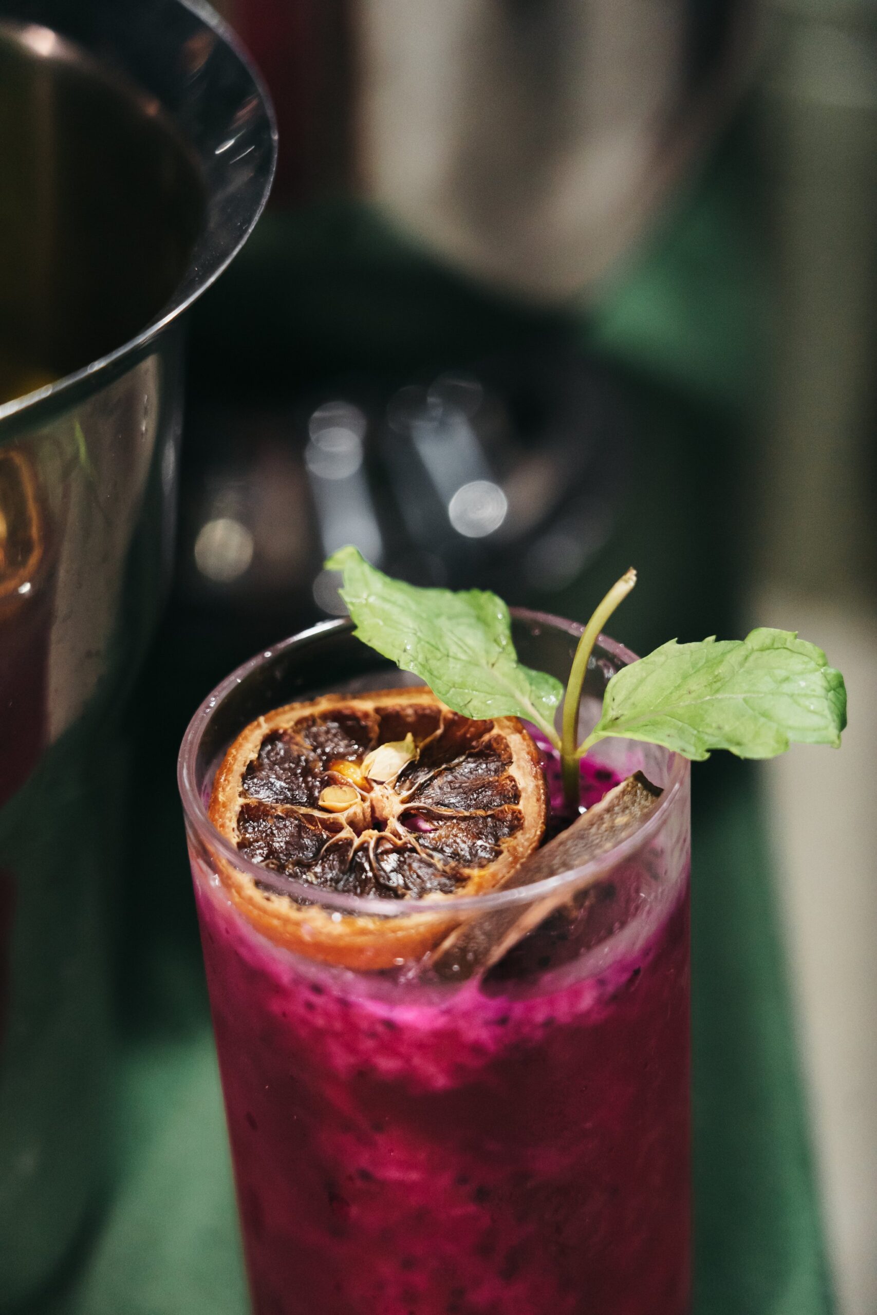 A vibrant magenta cocktail garnished with a dehydrated citrus slice and fresh mint leaves, being poured aboard the untamed amazon cruise