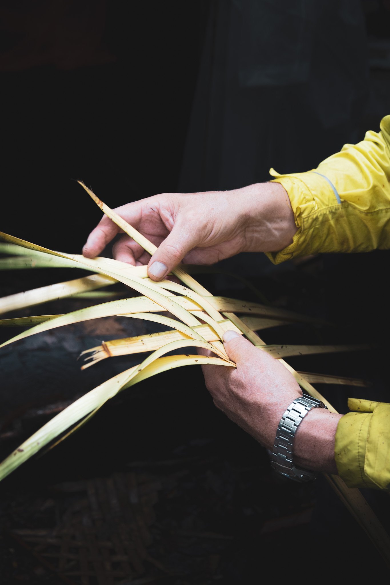 Hands weaving thin palm leaf strips during a jungle survival demonstration in the Amazon