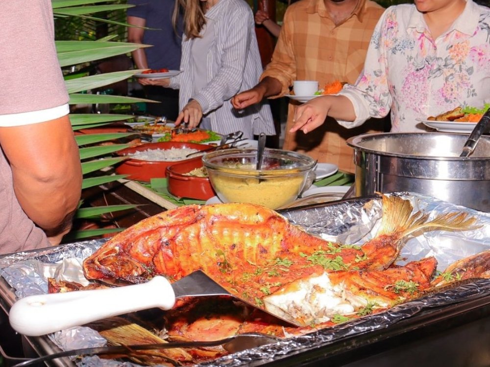 Whole roasted tambaqui fish on a serving tray as guests fill their plates at an Amazon lodge buffet