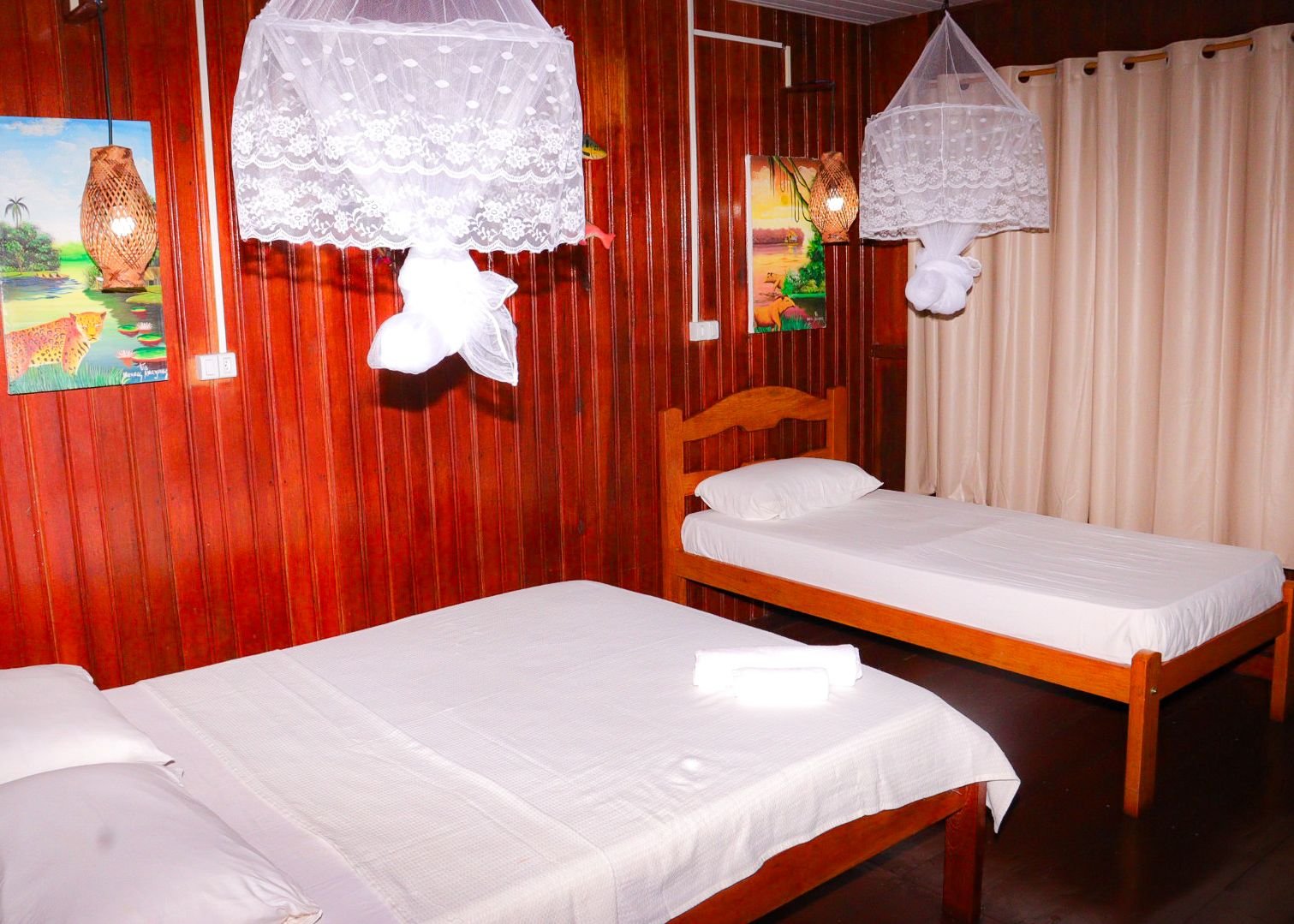 Double and single beds under nets make the wooden bungalow ideal for families. Wooden bungalow room with a double and a single bed under mosquito nets in the Amazon